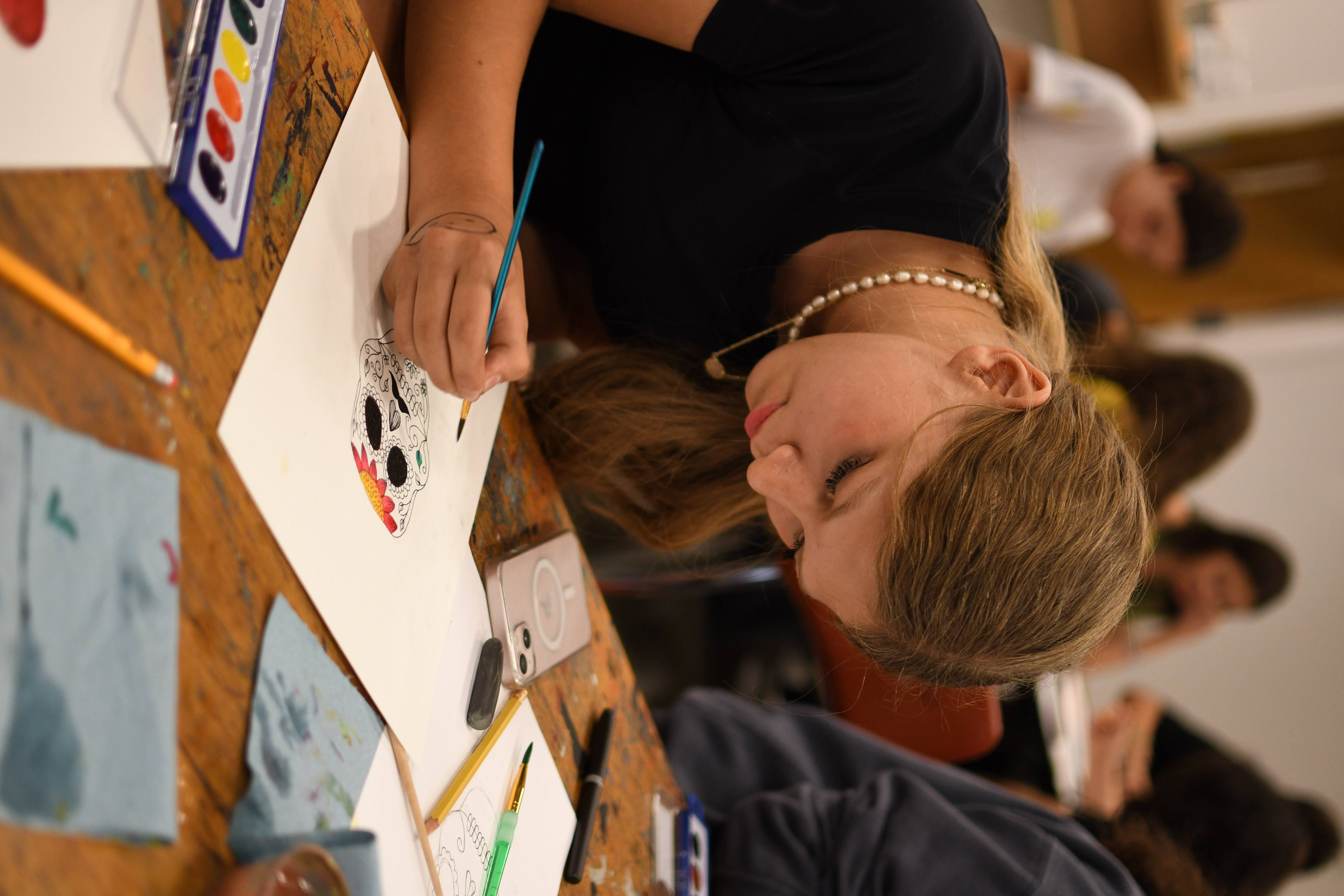 Student carefully painting a sugar-skull illustration with watercolors