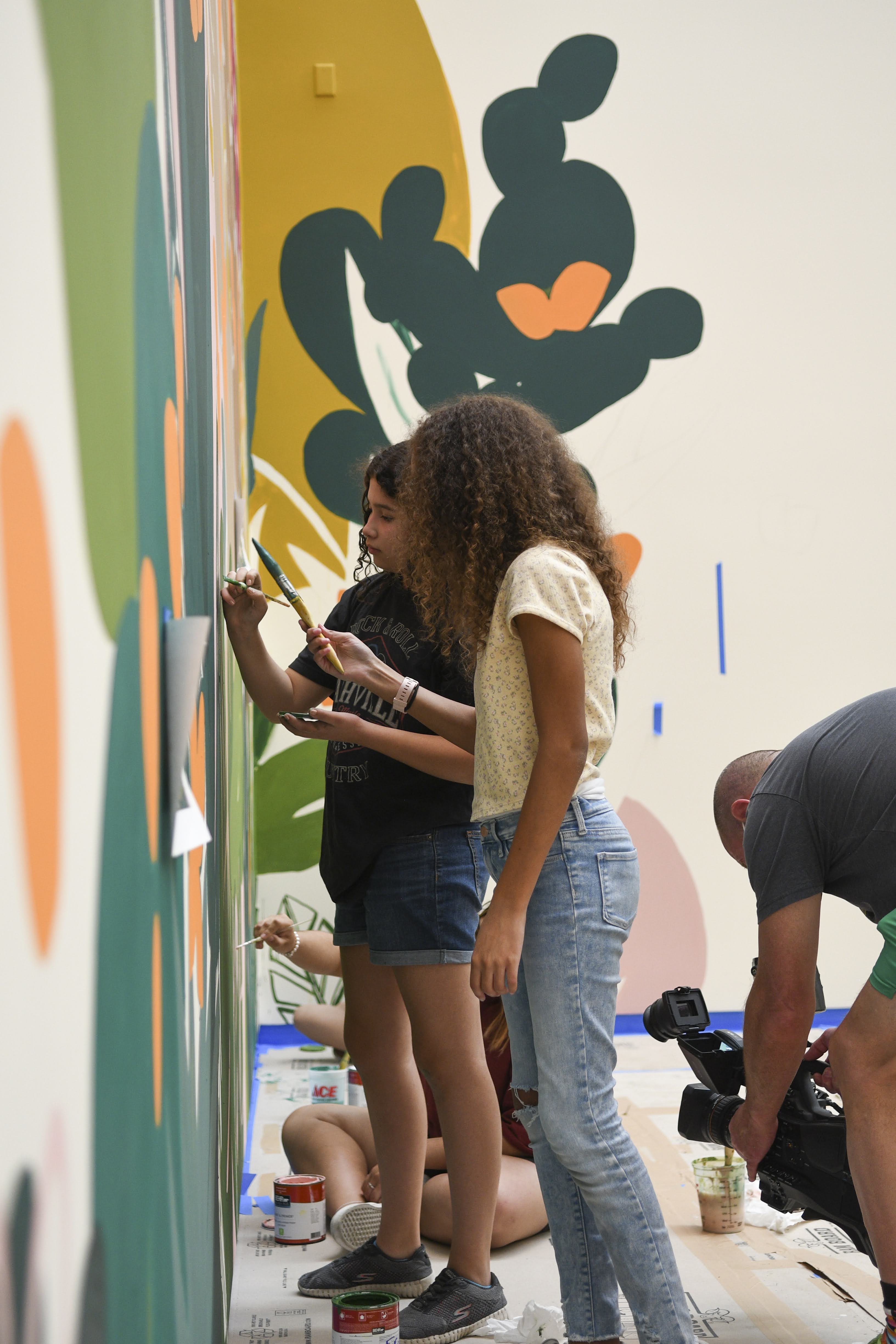 Students painting details on a large colorful mural with plants and abstract shapes
