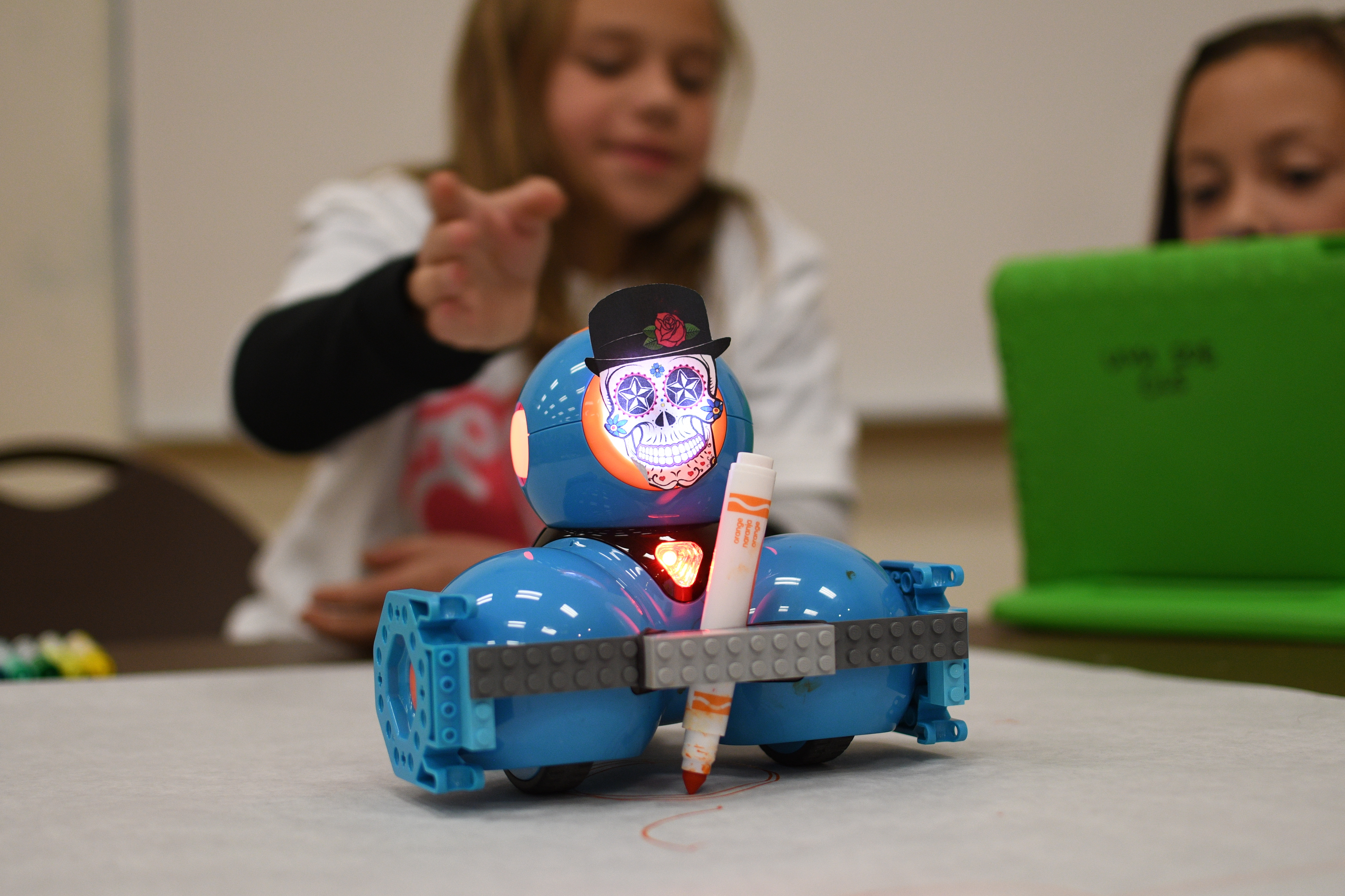 Small blue robot decorated with a Día de los Muertos skull drawing while holding a marker
