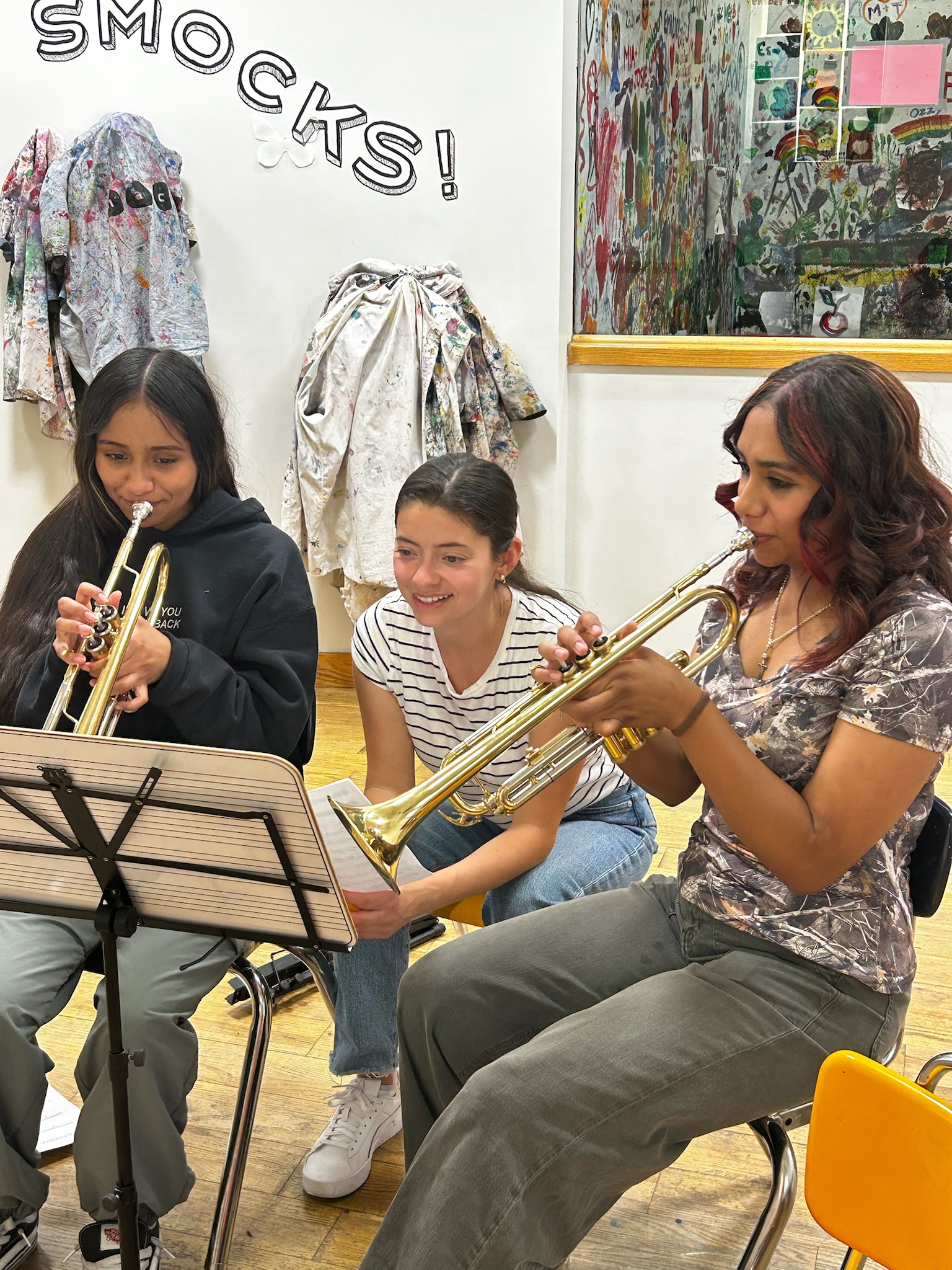 Mentor kneeling beside mariachi students as they practice trumpet together